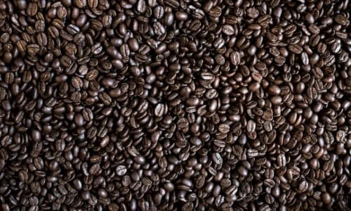 Pile of richly dark roasted coffee beans filling the frame, showcasing texture and deep brown colors for premium coffee brands.