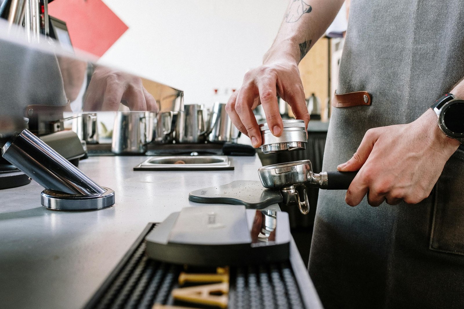 Close-up of a barista tamping coffee grounds with a portafilter in a café setting.