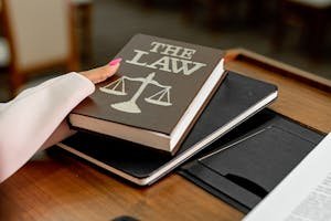 Closeup image of a law book titled 'The Law' on a wooden desk with scales of justice.