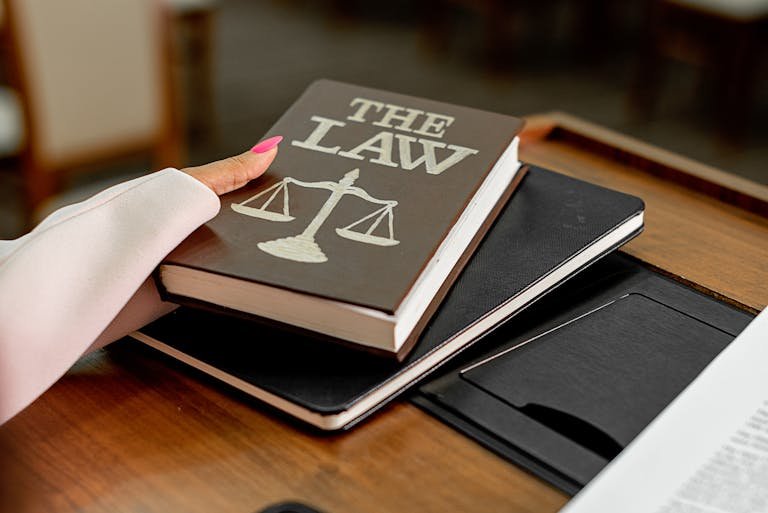 Closeup image of a law book titled 'The Law' on a wooden desk with scales of justice.