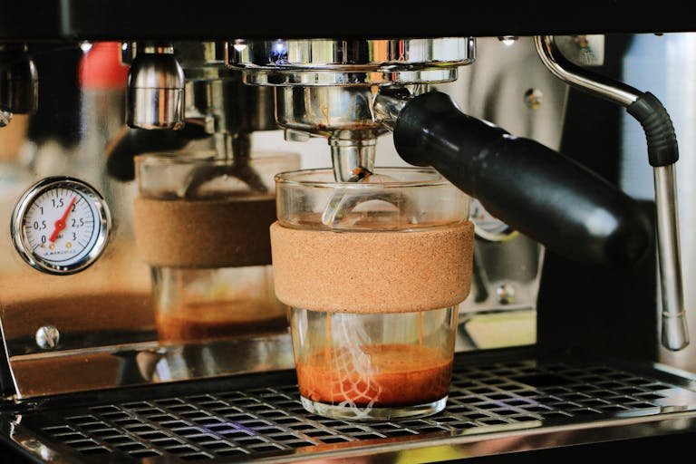 Espresso brewing in a glass cup with a cork holder, highlighting a coffee machine in action.