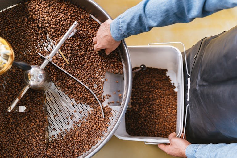 Hands delicately managing freshly roasted coffee beans in a roaster from a top view.