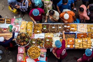 A busy street food market with people buying diverse foods from vendors.